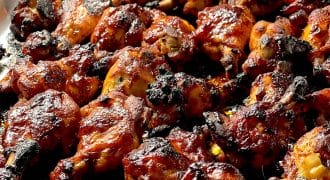 Barbecue chicken wings covered in a glossy, caramelised sauce, slightly charred, arranged closely together on a foil-lined baking tray.
