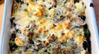 A baked casserole dish filled with broccoli, cauliflower, and melted cheese, browned on top, sitting on a wooden surface.