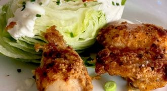 A plate with a wedge of iceberg lettuce topped with creamy dressing, chopped chives, and tomato, served alongside two pieces of crispy fried chicken.