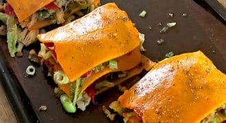 Three servings of vegetable lasagne made with orange squash slices instead of pasta sheets, layered with various vegetables, placed on a dark baking tray.