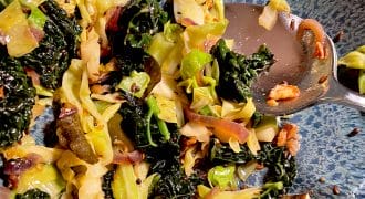 Sautéed cabbage and kale with onions and garlic in a blue speckled bowl, partially eaten, with a metal spoon resting on the side.