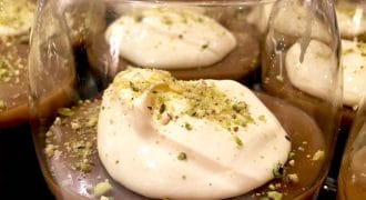 Glasses filled with chocolate mousse, each topped with a dollop of whipped cream and sprinkled with crushed pistachios.