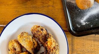 A plate of crispy breaded chicken pieces, a saucepan of green beans, and a baking tray with baked potatoes on a wooden table.