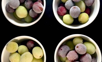 Four white bowls filled with green and purple grapes, some with a frosty appearance, arranged in a square pattern on a black background.