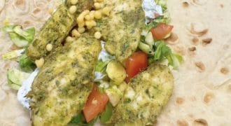 An open flatbread wrap topped with herbed chicken pieces, chopped lettuce, diced tomatoes, sweetcorn kernels, and a white sauce, ready to be folded.