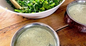 A bowl of chopped green salad with tongs next to two bowls of creamy green herb dressing on a wooden table.