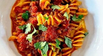 A white bowl filled with fusilli pasta topped with chunky tomato sauce and garnished with fresh parsley leaves, placed on a wooden surface.