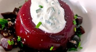 A round serving of beet jelly topped with a dollop of herbed cream sits on a plate, surrounded by small diced beetroot and sprinkled with fresh chives.