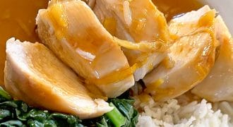 Sliced chicken breast drizzled with brown sauce, served with steamed white rice and leafy cooked greens on a white plate.