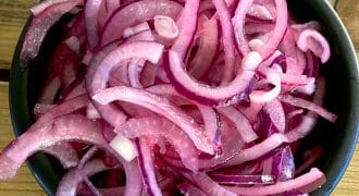 A black bowl filled with thinly sliced red onions, placed on a wooden surface.