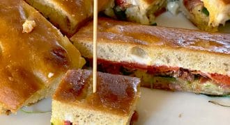 A close-up of sliced focaccia sandwiches with fillings such as vegetables and cheese, served on a white plate. One small sandwich piece is secured with a cocktail stick.