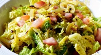 A decorative bowl filled with a fresh salad made of chopped leafy greens, caramelised onions, and diced pink vegetables, possibly apples or tomatoes. The salad is lightly tossed and appears crisp and colourful.