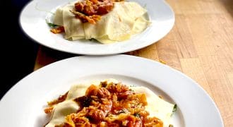 Three white plates sit on a wooden counter, each with homemade lasagne featuring visible pasta sheets and a chunky tomato-based sauce with meat and vegetables, ready to be served.