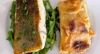 A white plate with a piece of fish with crispy skin and chopped chives, served on green beans, next to a slice of cheesy potato gratin.