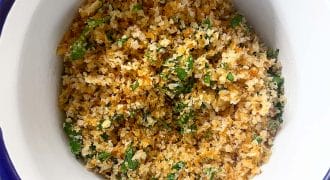 A white bowl with a blue rim filled with golden-brown seasoned breadcrumbs mixed with chopped green herbs, sitting on a wooden surface.