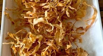 A tray lined with kitchen paper holds a pile of crispy, golden-brown parsnip crisps, freshly cooked and lightly seasoned.