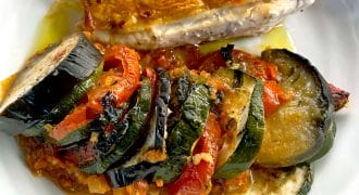 A plate with a sliced, golden-brown roasted chicken breast and a serving of colourful ratatouille made with courgette, aubergine, and tomatoes, all arranged neatly on a white dish.