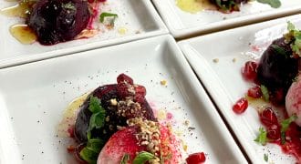Four rectangular plates each with a vibrant salad of roasted beetroot, creamy cheese, pomegranate seeds, herbs, crushed nuts, and a drizzle of dressing, artfully arranged for serving.