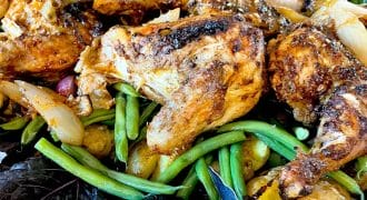 A plate of roast chicken pieces served on a bed of green beans, new potatoes, onions, and leafy greens, garnished with herbs.