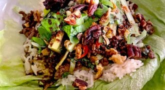 A lettuce leaf filled with white rice, minced meat, chopped spring onions, pecans, and assorted vegetables, served as a wrap.