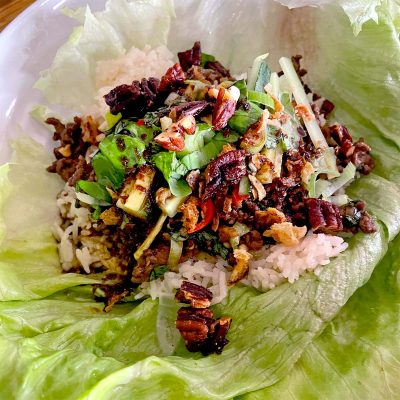 A lettuce leaf filled with white rice, minced meat, chopped spring onions, pecans, and assorted vegetables, served as a wrap.