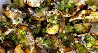 A plate of baked potato skins topped with melted cheese and chopped spring onions, arranged closely together on a white dish.