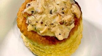 A golden, round puff pastry case filled with a creamy, mushroom and herb sauce, served on a white plate.