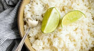 A bowl of white rice topped with two lime wedges, with a silver fork resting at the side. The bowl is placed on a grey and white striped cloth.